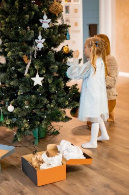 Anne ve çocuklar Noel ağacını çelenkler ve oyuncaklarla süsler. Aile Noel ağacını süslüyor. Noel ve Yeni Yıl için hazırlanıyorum. Çocuklar ağaca sevinir..