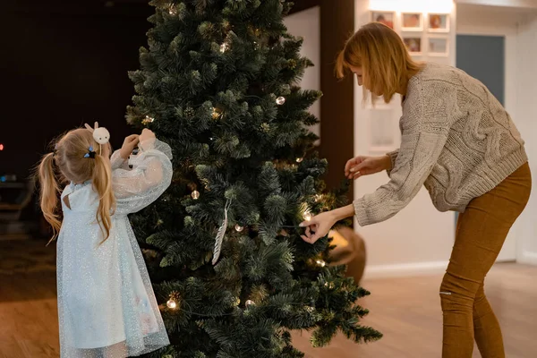 Mom and children decorate the Christmas tree with garlands and toys. The family decorates the Christmas tree. Preparing for Christmas and New Years. Children rejoice at the tree.