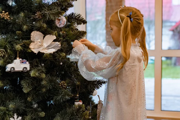 Een Klein Meisje Versiert Een Kerstboom Met Bloemenslingers Speelgoed Kinderen — Stockfoto