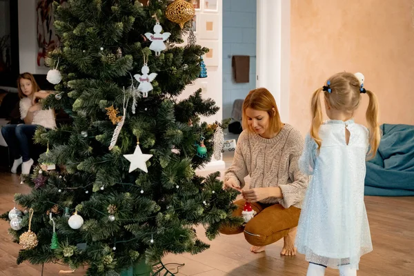 妈妈和孩子们用花环和玩具装饰圣诞树 这家人装饰圣诞树 为圣诞节和新年做准备 孩子们为这棵树感到高兴 — 图库照片