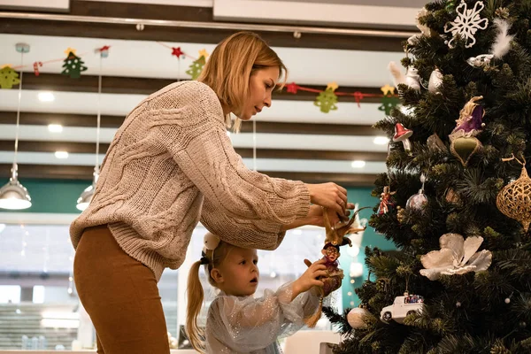 Mom and children decorate the Christmas tree with garlands and toys. The family decorates the Christmas tree. Preparing for Christmas and New Years. Children rejoice at the tree.