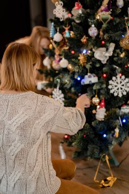 Genç bir kadın Noel ağacını çelenkler ve oyuncaklarla süslüyor. Noel ve Yeni Yıl için hazırlanıyorum. Mutlu Noeller ve mutlu yıllar konsepti.