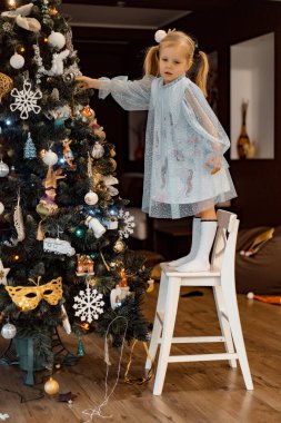 Küçük bir kız Noel ağacını çelenkler ve oyuncaklarla süslüyor. Çocuklar Noel ve Yeni Yıl için hazırlanıyorlar. Mutlu Noeller ve mutlu yıllar konsepti.