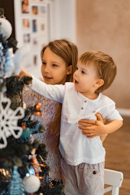 Çocuklar Noel ağacını süsler, erkek ve kız kardeşler tatil için evi dekore ederler. Noel tatili. Mutlu Noeller ve mutlu yıllar konsepti.