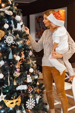 Anne ve çocuklar Noel ağacını çelenkler ve oyuncaklarla süsler. Aile Noel ağacını süslüyor. Noel ve Yeni Yıl için hazırlanıyorum. Çocuklar ağaca sevinir..