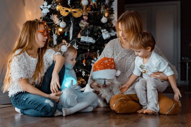 Mutlu aile Noel ağacının yanında eğleniyor, Noel 'de. Çocuklu bir anne ve Noel ağacında bir köpek. Kız ve erkek kardeşler, üç çocuk.