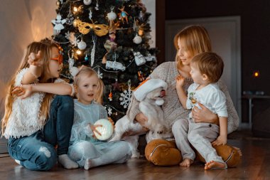 Mutlu aile Noel ağacının yanında eğleniyor, Noel 'de. Çocuklu bir anne ve Noel ağacında bir köpek. Kız ve erkek kardeşler, üç çocuk.