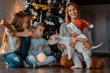 Mutlu aile Noel ağacının yanında eğleniyor, Noel 'de. Çocuklu bir anne ve Noel ağacında bir köpek. Kız ve erkek kardeşler, üç çocuk.