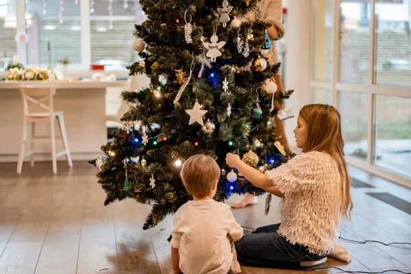 Children decorate the Christmas tree, brother and sister decorate the house for the holidays. Christmas holidays. Merry Christmas and Happy New Year concept.