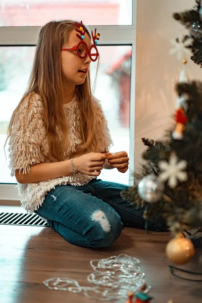 小さな女の子がガーランドやおもちゃでクリスマスツリーを飾ります 子供たちはクリスマスと新年の準備をしています メリークリスマスとハッピーニューイヤーのコンセプト — ストック写真