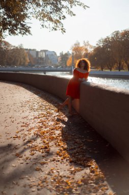 Kıvırcık siyah saçlı, kırmızı elbiseli güzel bir kadın sonbahar şehrinde yürüyor. Sonbahar havası, ayak altında sarı yapraklar.