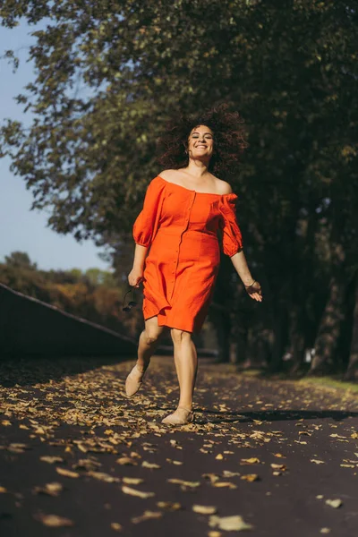 秋の街を歩くのは 赤いドレスの中に巻き毛の美しい女性 秋の気分 黄色の葉の足の下 — ストック写真