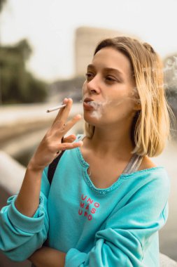 Genç ve güzel bir kadın sigara içiyor. Şehir atmosferi, otomatik
