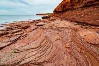Kanada 'nın Prens Edward Adası' ndaki Cavendish plajında, düz kırmızı kumtaşı, düşen kayalarla görülen erozyon yıllarının çizgilerini ortaya çıkarmak için rüzgarlar ve okyanus akıntıları tarafından aşınmıştır.. 