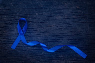 Koyu mavi kurdeleli, eski, ahşap arka planda. Kolon kanseri ve Renkli Kanser Farkındalığı. Sağlık ve Tıp Konsepti.