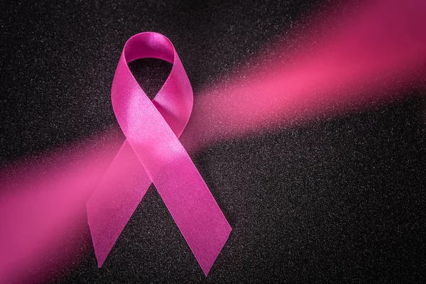 Pink ribbon on vignet glitter black background and blurred pinkband, Breast cancer awareness symbol, October Pink day background, world cancer day.