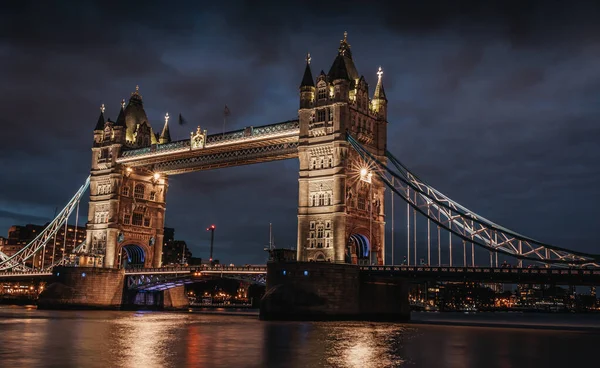 tower bridge illuminated at night with intense and dark clouds. tower bridge lit above the thames river in the dark and cloudy night