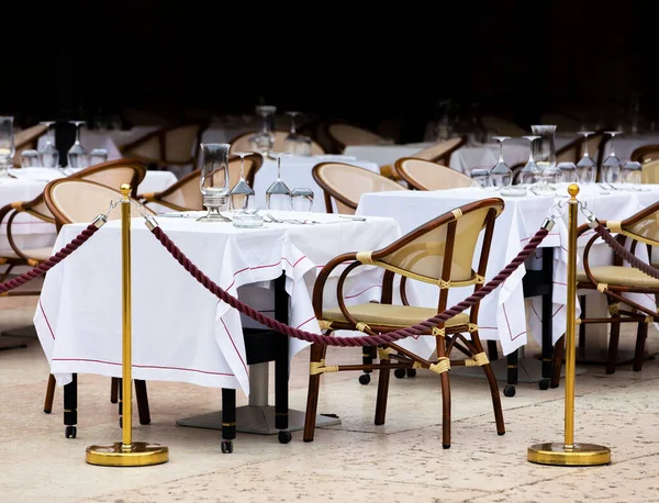 Elegant outdoor terrace with white tablecloth and glass glasses turned upside down. Yellow iron bars with brown protective rope in front