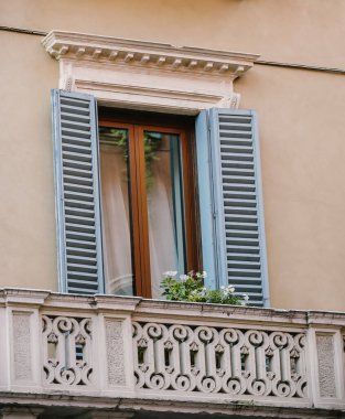Yeşil çiçeklerle süslenmiş eski model balkon. Yeşil ahşap panjurlu kahverengi pencere. Eski antika balkon