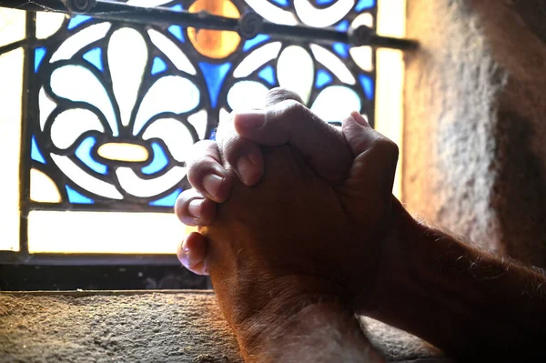 Duas mãos rezando em uma igreja atrás de uma janela Imagem De Stock