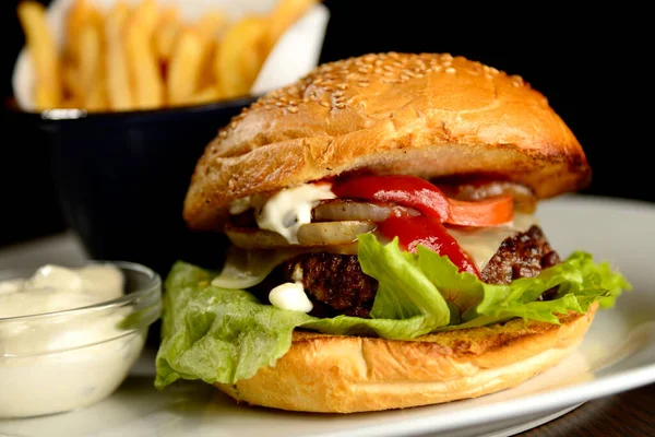 Patates kızartmalı hamburger ve siyah arkaplanda sos.