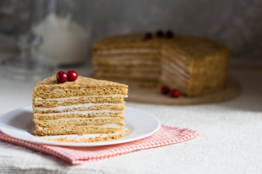 Beyaz tabakta kirazla süslenmiş katmanlı kremalı ballı kek.