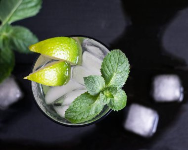 Limonlu mojito kokteyli, nane yeşili ve siyah ahşap masada buz. Üst görünüm, seçici odak