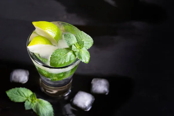 Mojito cocktail with lime, mint green and ice on dark wooden table, selective focus