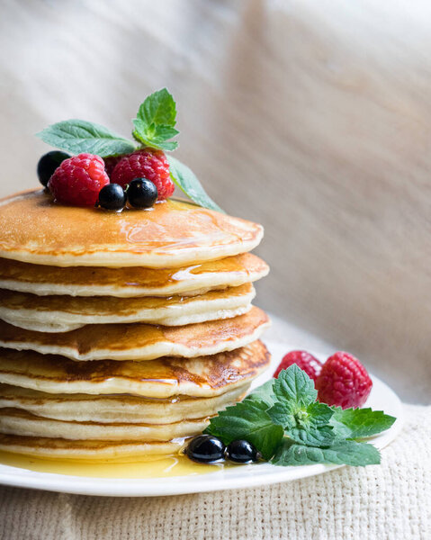 American classic pancakes with raspberry, black currant, honey and mint on a light textile background, selective focus.