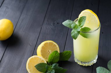 Limon ve nane dilimli bir bardak limonata, soğuk ferahlatıcı içecek ya da koyu ahşap arka planda buzlu içecek. Seçici odak.