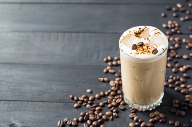 Bir bardak buzlu kahve, kahve çekirdekleri ve siyah ahşap masada buz küpleri. Seçici odaklanma. Uzayı kopyala Yatay yönelim