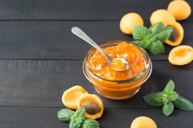 Cam kavanozda kayısı reçeli. Koyu ahşap masada olgun kayısılar, seçici odak, yatay yönelim.