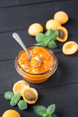 Cam kavanozda kayısı reçeli ve koyu ahşap bir masa üzerinde olgun kayısılar, seçici odak, dikey yönelim