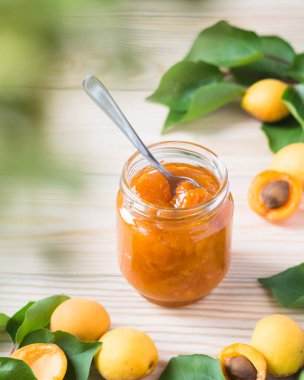 Cam kavanozda kayısı reçeli ve ahşap kırsal masada olgun kayısılar, seçici odak, dikey yönelim