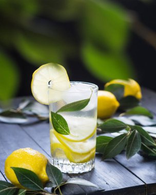 Yaz içeceği. Limon dilimli limonata ve siyah ahşap arka planda taze limonlar, seçici odak, dikey yönelim.