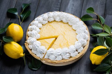 Ev yapımı limonlu turta, dilimlenmiş parça, siyah ahşap arka planda taze limonlar, seçici odak, yatay yönelim.