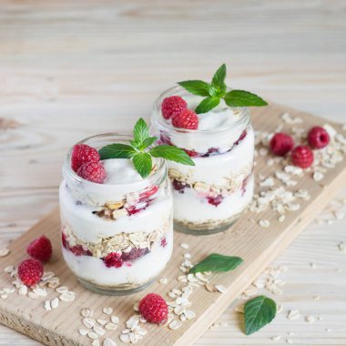 İki porsiyon ev yapımı doğal yoğurt yulaf ezmesi ve cam kavanozlarda taze ahududu. Seçici odaklanma. Sağlıklı kahvaltı kavramı.