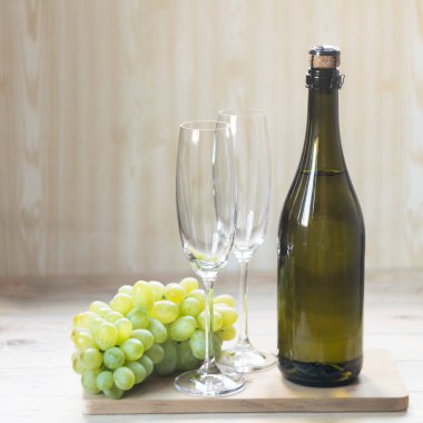 Bir şişe köpüklü şarap, iki bardak ve hafif ahşap arka planda bir demet üzüm. Seçici odak.