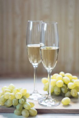 İki bardak köpüklü şarap ve hafif ahşap arka planda üzümler. Seçici odak.