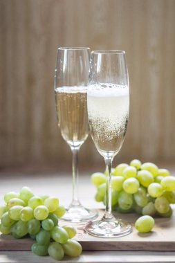 İki bardak köpüklü şarap ve hafif ahşap arka planda üzümler. Seçici odak.