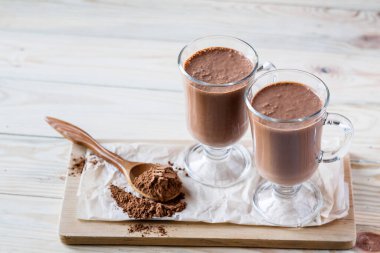 Kahve sütlü macchiato ya da tahta arka planda iki bardak sıcak çikolata, kakao tozlu bir kaşık. Seçici odak, kopyalama alanı