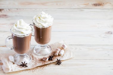 Hafif ahşap arka planda çırpılmış kremalı iki bardak kakao. Seçici odak, kopyalama alanı.