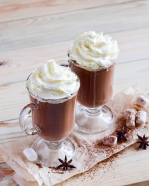 Hafif ahşap arka planda çırpılmış kremalı iki bardak kakao. Seçici odak.