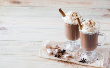 Hafif ahşap arka planda çırpılmış kremalı iki bardak kakao. Seçici odaklanma. Kopyalama alanı