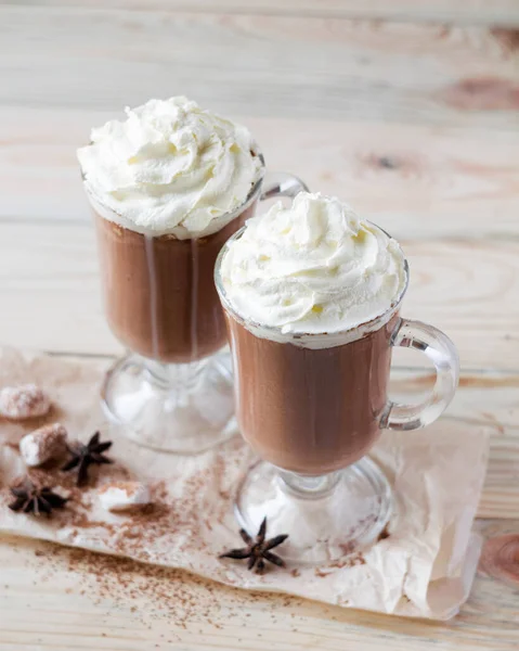 Hafif ahşap arka planda çırpılmış kremalı iki bardak kakao. Seçici odak.