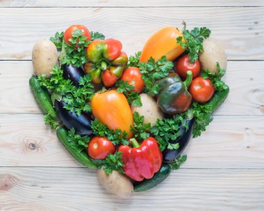 Hafif ahşap arka planda kalp şeklinde taze organik sebzeler. Vegan ve sağlıklı beslenme konsepti