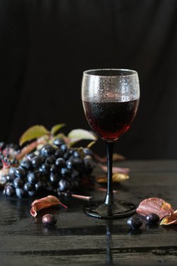 Siyah arka planda üzüm ve yapraklı bir kadeh kırmızı şarap, seçici odaklı.