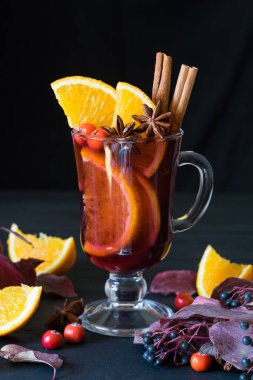 Sonbahar yapraklı, portakal dilimli ve böğürtlenli siyah ahşap zemin üzerinde sıcak şarap ve baharatlar. Seçici odak.