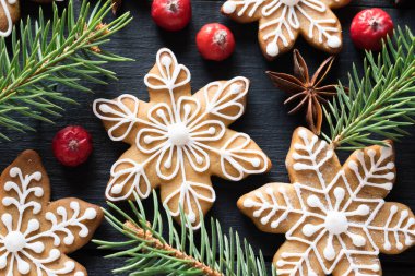 Zencefilli kurabiyeler köknar ağacı dallarıyla süslenmiş kar taneleri ve siyah ahşap arka planda böğürtlenler. Yakın plan.