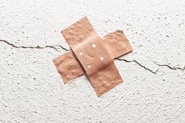 band-aid plaster in cross shape on a crack in the wall, concept for botched construction and doctoring around symptoms, copy space clipart